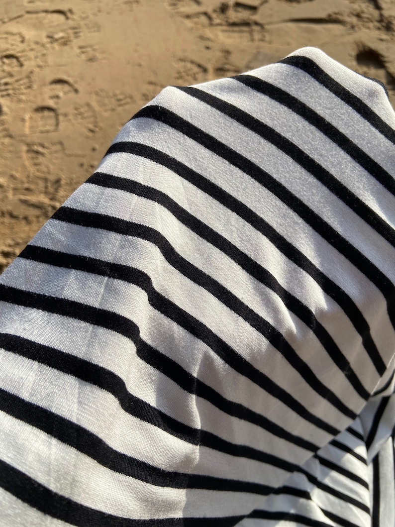 May include: Close-up of a white and black striped fabric. The fabric is soft and has a subtle sheen.