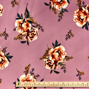 May include: A close-up of a dusty rose fabric with a floral pattern. The fabric features a repeating pattern of beige and brown flowers with green leaves. A ruler is visible at the bottom of the image.