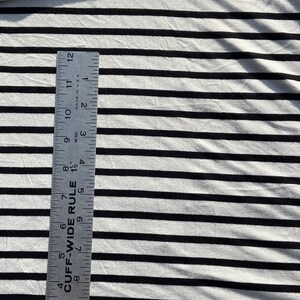 May include: White and black striped fabric with a ruler measuring 12 inches. The ruler is labeled "CUFF-WIDE RULE" and has markings in inches and fractions of an inch.