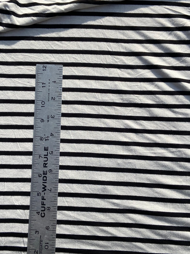 May include: White and black striped fabric with a ruler measuring 12 inches. The ruler is labeled "CUFF-WIDE RULE" and has markings in inches and fractions of an inch.
