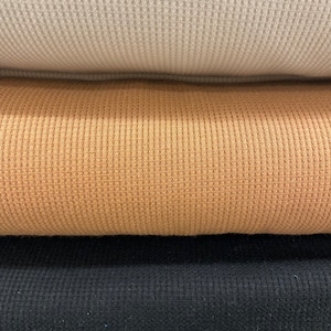 May include: Close-up of three stacked fabric swatches. The top swatch is a light beige waffle knit, the middle is a tan waffle knit, and the bottom is a black waffle knit. The fabric has a textured, grid-like pattern.