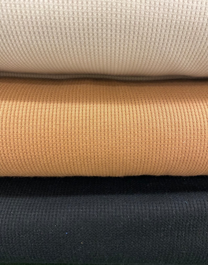 May include: Close-up of three stacked fabric swatches. The top swatch is a light beige waffle knit, the middle is a tan waffle knit, and the bottom is a black waffle knit. The fabric has a textured, grid-like pattern.