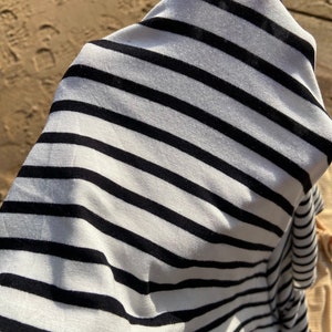 May include: A white and black striped fabric with a soft, textured feel. The fabric is folded and draped over a surface.