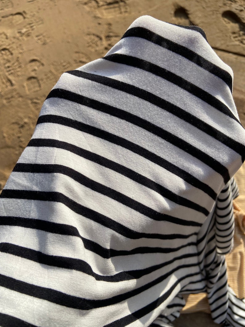 May include: A white and black striped fabric with a soft, textured feel. The fabric is folded and draped over a surface.