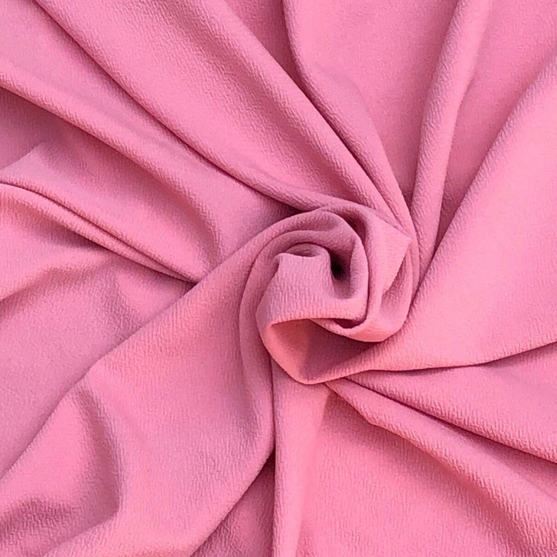 May include: A solid pink fabric with a distinct crepe texture, featuring deep folds and a central swirl that creates natural shadows and highlights across the surface, showcasing the consistent color and the fine, pebbled grain of the material.