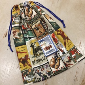 May include: Drawstring bag with a vintage sports poster print. The bag features a blue drawstring closure and is patterned with various sports-themed graphics in shades of yellow, green, red, and white. The bag is made of fabric.
