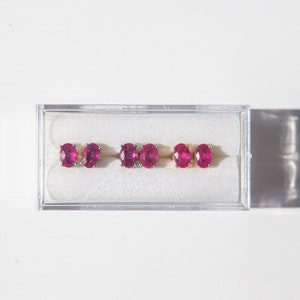 May include: Three pairs of ruby earrings in a clear plastic box. The earrings are oval shaped and set in gold.