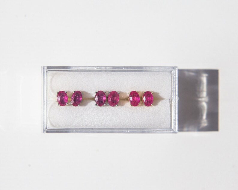 May include: Three pairs of ruby earrings in a clear plastic box. The earrings are oval shaped and set in gold.