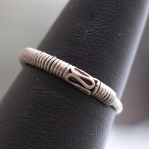 May include: A silver ring with a textured band and a decorative design on the top.