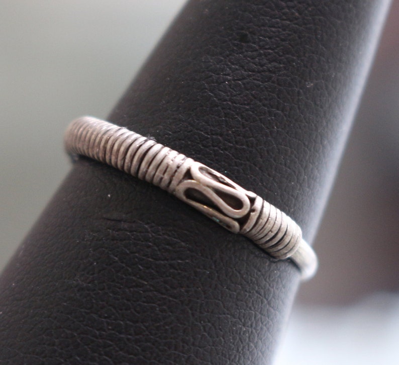 May include: A silver ring with a textured band and a decorative design on the top.