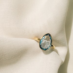 May include: A gold ring with a light blue teardrop-shaped gemstone.