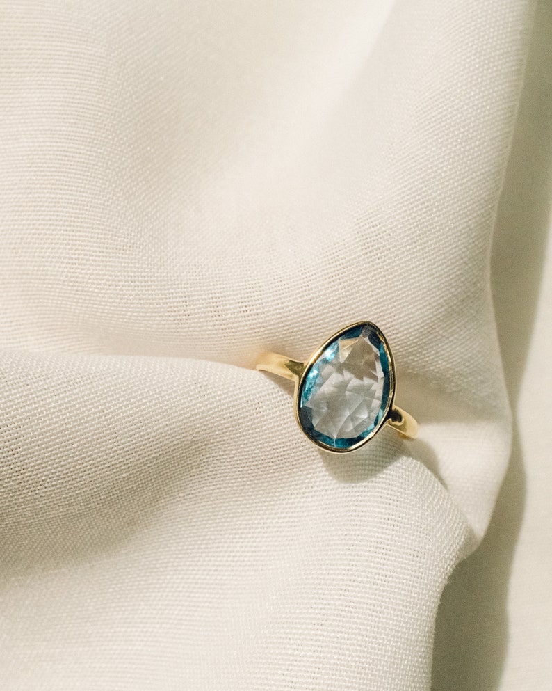 May include: A gold ring with a light blue teardrop-shaped gemstone.