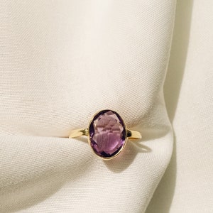 May include: A gold ring with a large, oval-shaped amethyst gemstone.