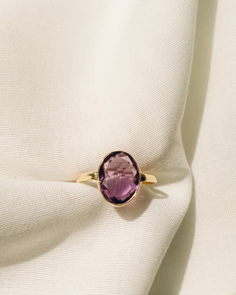 May include: A gold ring with a large, oval-shaped amethyst gemstone.