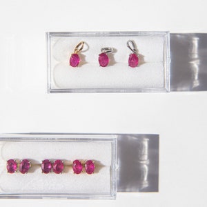 May include: Three pairs of ruby earrings in clear plastic boxes. The earrings are oval shaped and have a silver or gold setting.