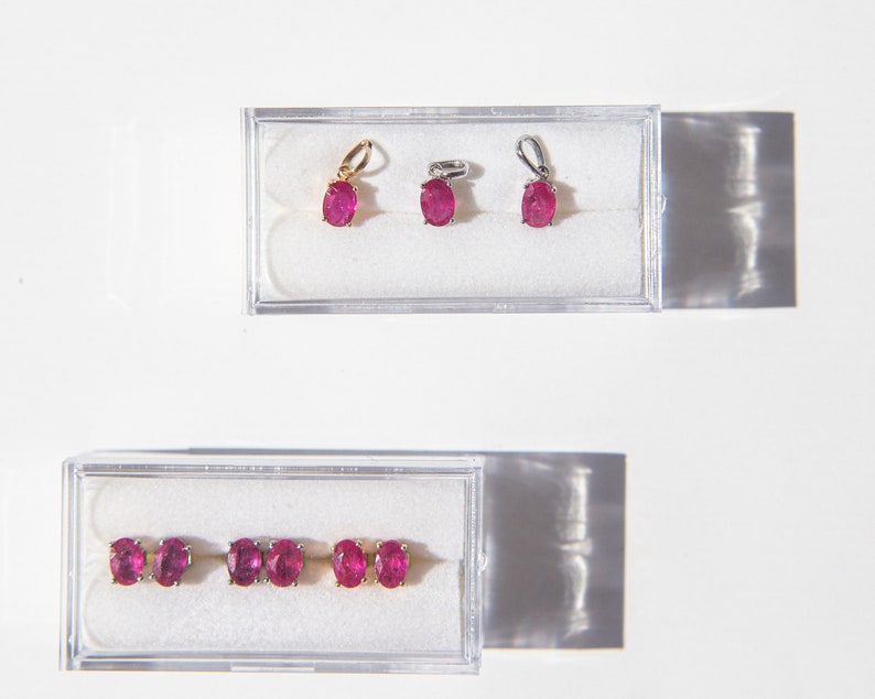 May include: Three pairs of ruby earrings in clear plastic boxes. The earrings are oval shaped and have a silver or gold setting.
