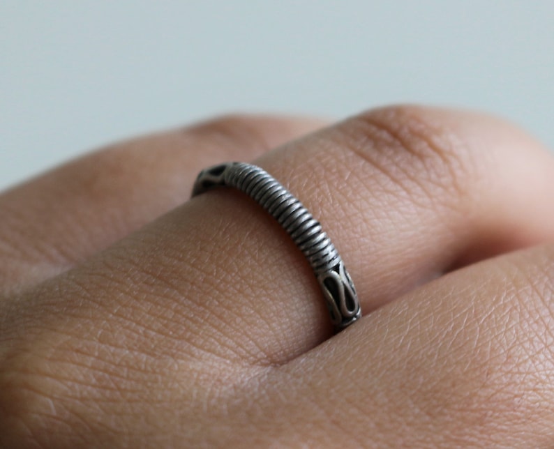 May include: A silver ring with a textured, twisted band. The band has a decorative design at the top.