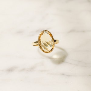 May include: A gold ring with a large, oval-shaped, faceted, light yellow gemstone.