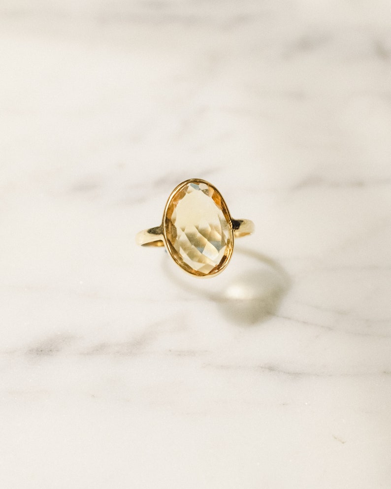 May include: A gold ring with a large, oval-shaped, faceted, light yellow gemstone.