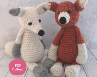 May include: Two crocheted fox plushies, one white with gray accents and one orange with white accents. The plushies are sitting on a white wooden surface. The text "PDF Pattern" is visible in the lower left corner of the image.