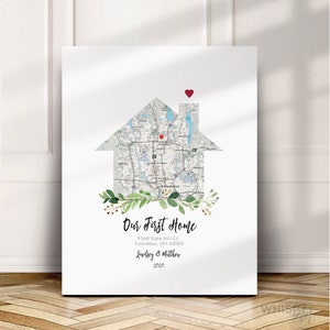 May include: A white canvas print with a map of Columbus, Ohio, shaped like a house. The map is surrounded by green leaves and a red heart is placed on the house. The text "Our First Home", "9568 Slate Hill Ct., Columbus, OH 43085", "Lindsey & Matthew", and "2020" is printed below the house.
