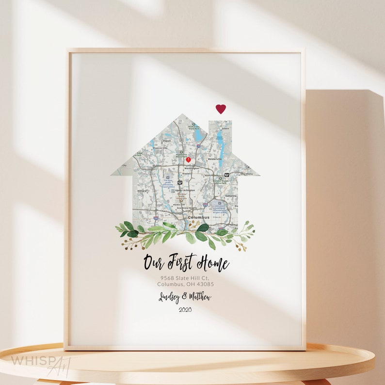 May include: A white printable art print with a map of Columbus, Ohio, shaped like a house. The map is surrounded by green leaves and gold accents. The text "Our First Home" is below the map, along with the address, "9568 Slate Hill Ct., Columbus, OH 43085", and the names "Lindsey & Matthew" and the year "2020".