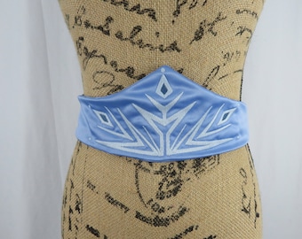 May include: A light blue satin belt with a white snowflake design. The belt is on a dress form.