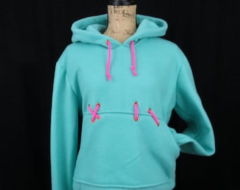 May include: A turquoise blue hoodie with a pink drawstring and gold grommets. The hoodie has a kangaroo pocket and a relaxed fit.