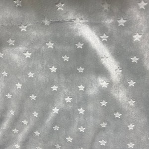 May include: A close-up of a soft, gray fabric with a pattern of white stars. The stars are evenly spaced across the surface of the fabric. The fabric has a velvety texture and a subtle sheen.