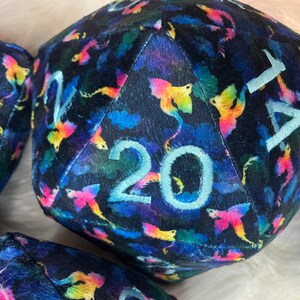 May include: A plush, black, 20-sided dice with a colorful, iridescent pattern of dragons. The numbers are embroidered in white.