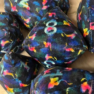 May include: A set of six plush dice with a dark blue background and a colorful, abstract pattern of birds. The dice are numbered 1, 2, 3, 4, 5, and 6.