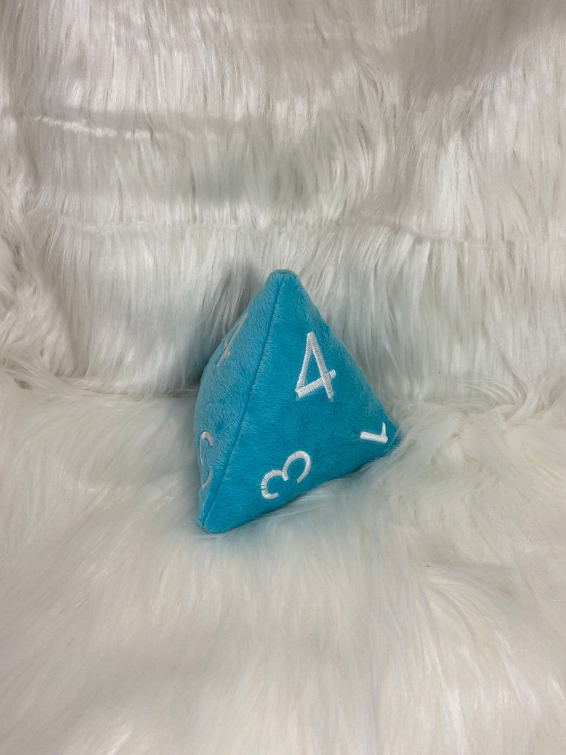 May include: A light blue plush dice with white numbers 1, 3, 4, and 5. The dice is a D4, or four-sided die.