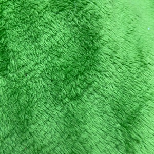 May include: Close-up of a soft, green, fuzzy fabric. The fabric has a slightly textured surface and a subtle sheen.