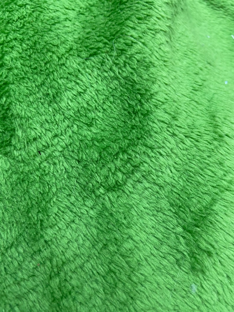May include: Close-up of a soft, green, fuzzy fabric. The fabric has a slightly textured surface and a subtle sheen.