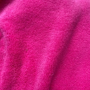 May include: Close-up of a soft, pink fabric with a fuzzy texture. The fabric is folded and has a slight sheen.