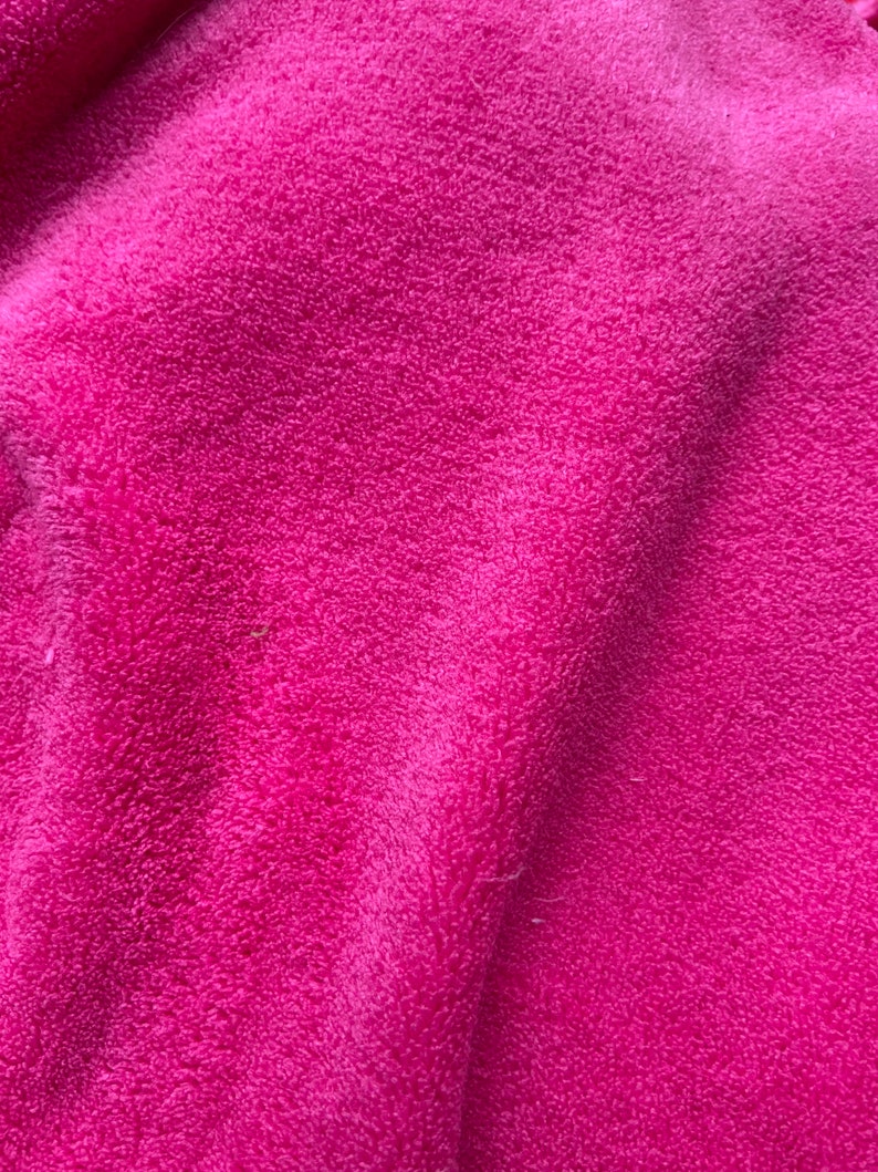 May include: Close-up of a soft, pink fabric with a fuzzy texture. The fabric is folded and has a slight sheen.
