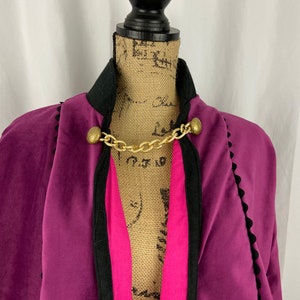 May include: A purple velvet cape with black trim and gold chain accents. The cape has a pink lining.