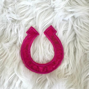 May include: A pink horseshoe-shaped patch with a glittery finish.