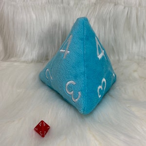 May include: A light blue plush dice with white numbers 2, 3, and 4 on each side. A red dice with white numbers 2, 3, and 4 is in the foreground.