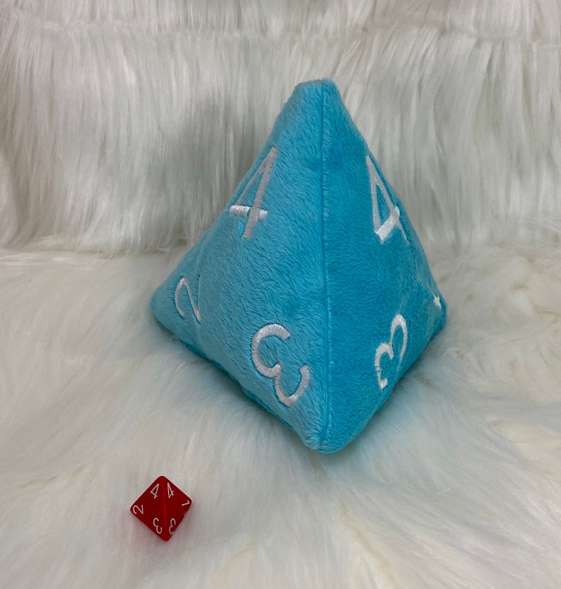 May include: A light blue plush dice with white numbers 2, 3, and 4 on each side. A red dice with white numbers 2, 3, and 4 is in the foreground.