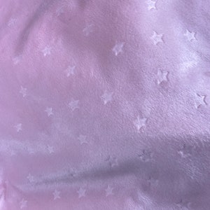 May include: A close-up of a soft, light pink fabric with a velvety texture. The fabric is patterned with small, embossed star shapes scattered across the surface. The lighting creates subtle shadows, enhancing the texture.