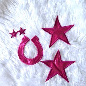 May include: Four pink felt patches, including two stars and a horseshoe, on a white fluffy surface.