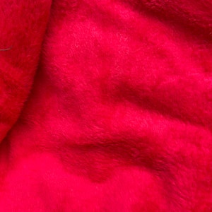May include: Close-up of a soft, red fabric with a fuzzy texture. The fabric is folded and has a slight sheen.