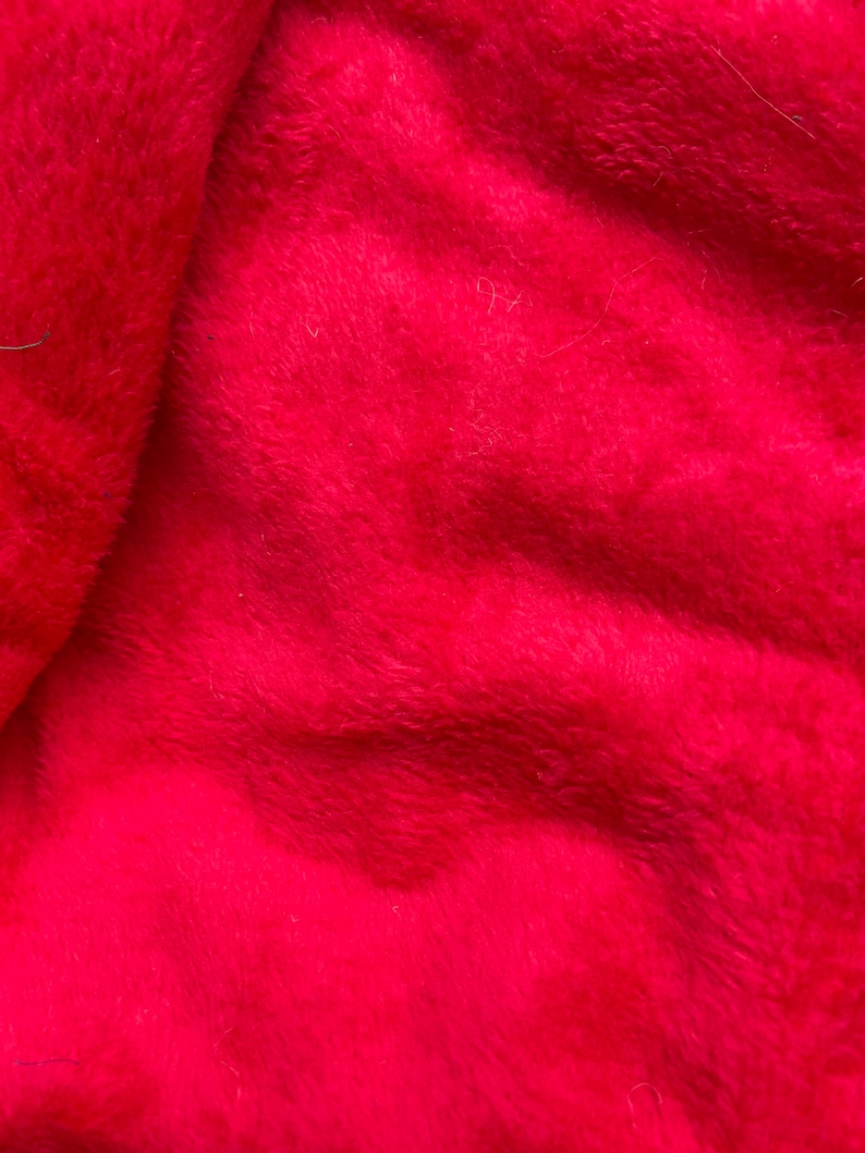 May include: Close-up of a soft, red fabric with a fuzzy texture. The fabric is folded and has a slight sheen.