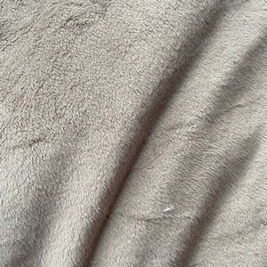 May include: Close-up of a soft, plush, gray fabric with a subtle texture. The fabric is folded, creating a diagonal line across the image.