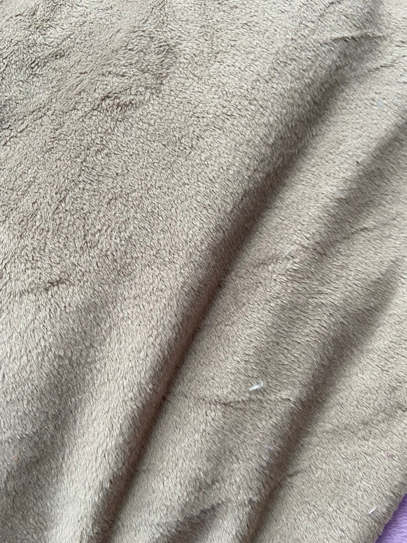 May include: Close-up of a soft, plush, gray fabric with a subtle texture. The fabric is folded, creating a diagonal line across the image.