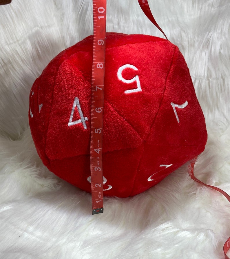 May include: A large, red, plush dice with white numbers 1, 2, 3, 4, 5, and 6. The dice is 7 inches tall.