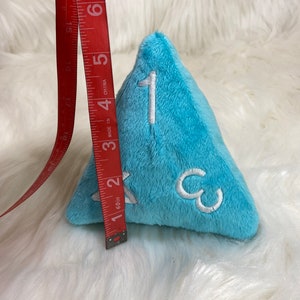 May include: A light blue plush dice with white numbers 1, 2, and 3. The dice is approximately 2 inches tall.