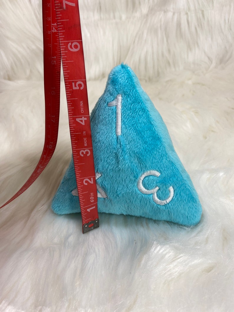 May include: A light blue plush dice with white numbers 1, 2, and 3. The dice is approximately 2 inches tall.