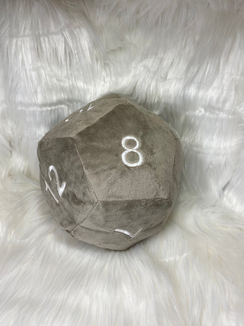 May include: A plush, gray, 12-sided die with white embroidered numbers. The soft, oversized gaming accessory is designed for tabletop role-playing games. The die is approximately 8 inches in diameter.
